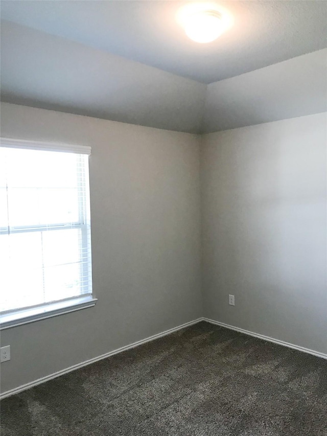 spare room featuring a healthy amount of sunlight, baseboards, dark carpet, and lofted ceiling