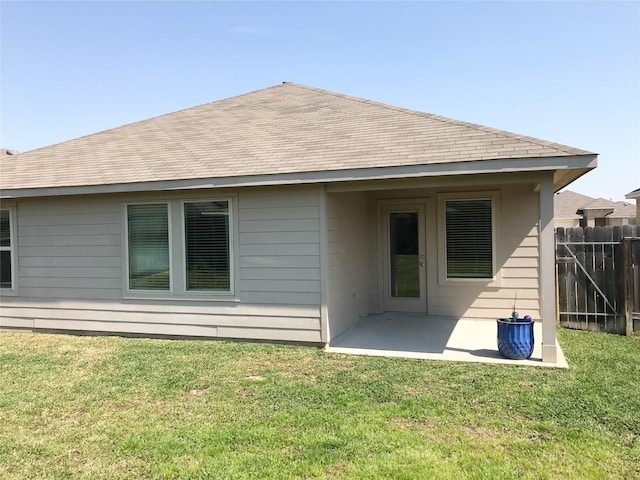 back of property with a yard, fence, a shingled roof, and a patio