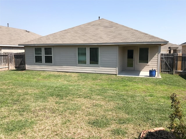 rear view of house with a fenced backyard, a lawn, and roof with shingles