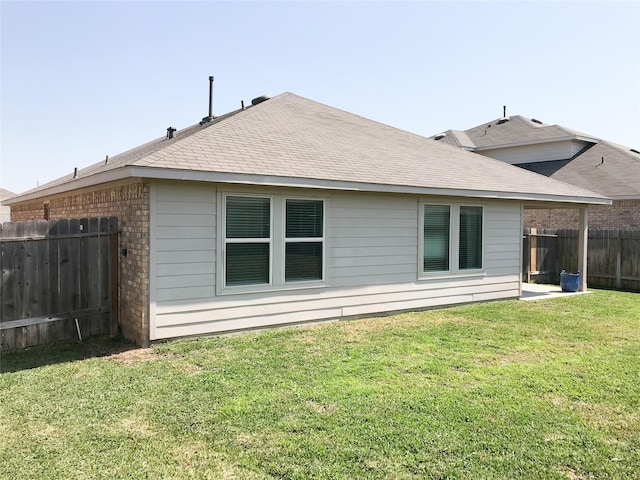 rear view of house featuring roof with shingles, brick siding, a lawn, and fence