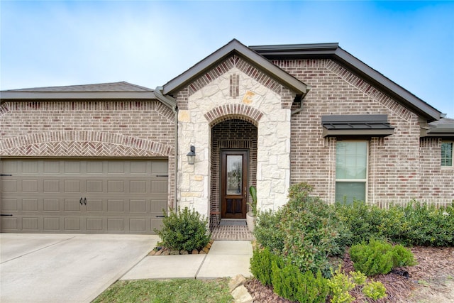 entrance to property featuring a garage, concrete driveway, brick siding, and stone siding