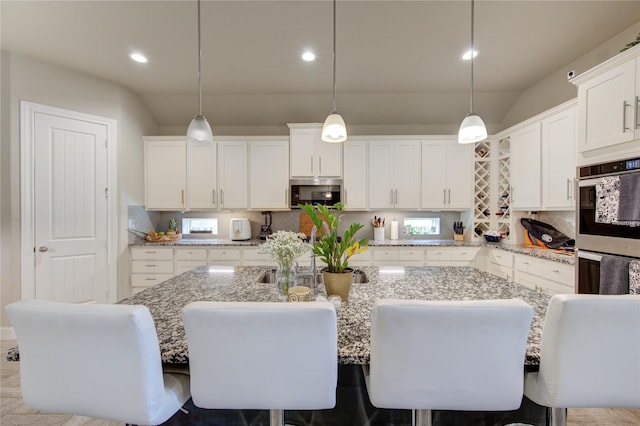 kitchen with light stone counters, decorative light fixtures, stainless steel appliances, a kitchen bar, and a center island with sink