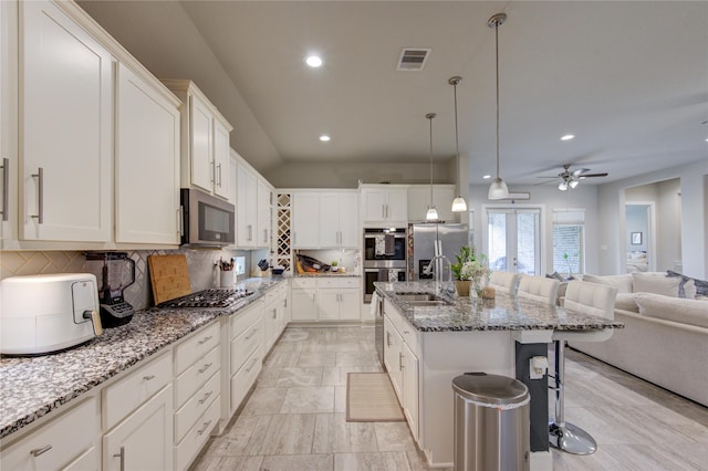 kitchen featuring a breakfast bar area, visible vents, open floor plan, appliances with stainless steel finishes, and a center island with sink