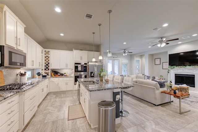 kitchen with light stone counters, stainless steel appliances, open floor plan, an island with sink, and pendant lighting