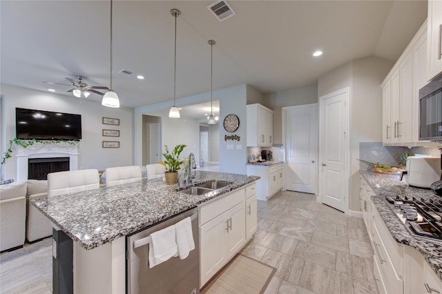 kitchen with stainless steel appliances, a kitchen island with sink, a sink, and white cabinetry