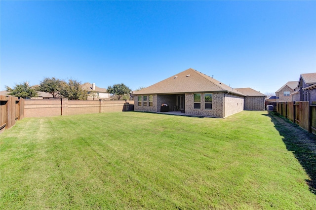 rear view of house featuring a yard, brick siding, and a fenced backyard