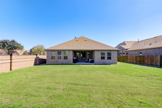 rear view of house with a yard, brick siding, and a fenced backyard