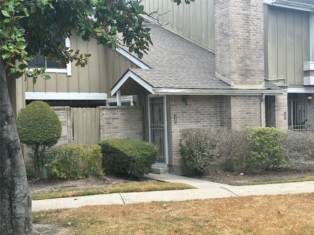 view of exterior entry featuring a shingled roof, a chimney, board and batten siding, and brick siding