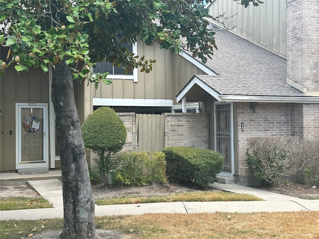 doorway to property featuring brick siding, a chimney, board and batten siding, and roof with shingles