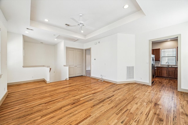 interior space with a raised ceiling, visible vents, attic access, a sink, and light wood-type flooring