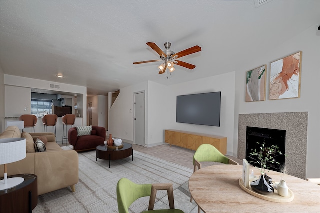 living area featuring light tile patterned floors, ceiling fan, a fireplace, and visible vents