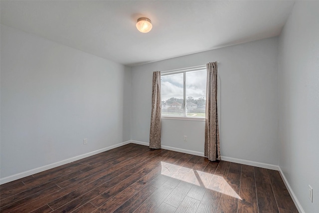 spare room featuring baseboards and dark wood-type flooring