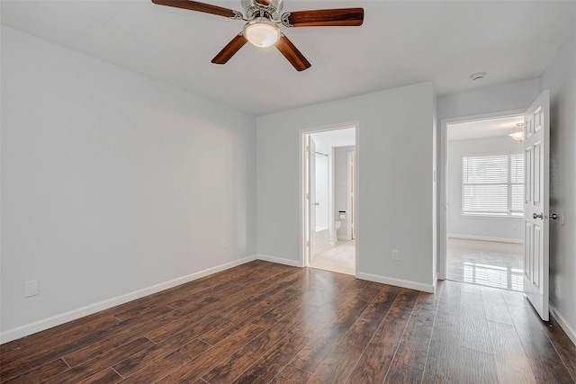 unfurnished bedroom with dark wood-style floors, ensuite bathroom, a ceiling fan, and baseboards