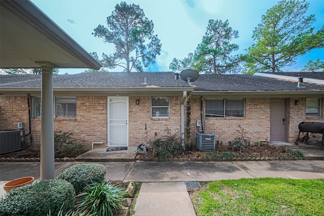 doorway to property with brick siding, roof with shingles, and cooling unit