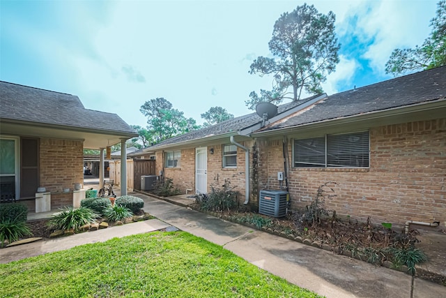 exterior space featuring cooling unit, brick siding, fence, and a front yard