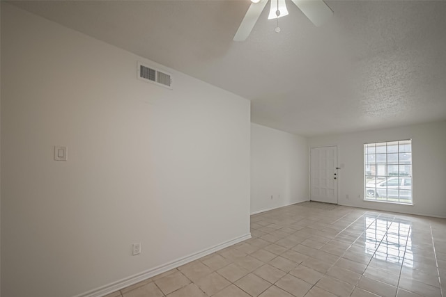 empty room featuring a textured ceiling, ceiling fan, light tile patterned flooring, visible vents, and baseboards