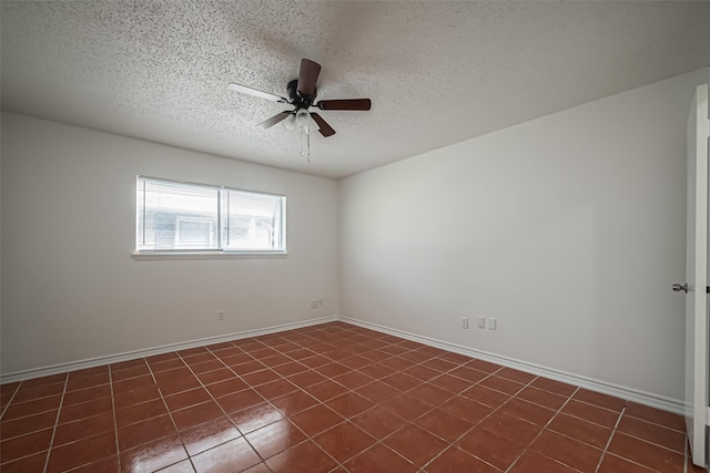 empty room featuring a textured ceiling, dark tile patterned floors, a ceiling fan, and baseboards