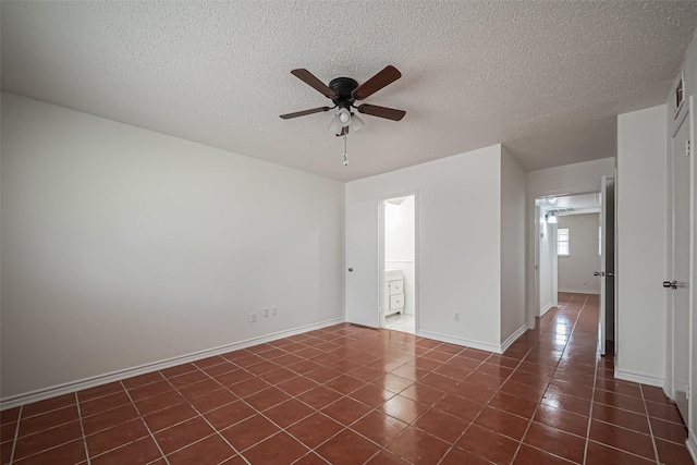 spare room featuring dark tile patterned floors, a textured ceiling, baseboards, and a ceiling fan