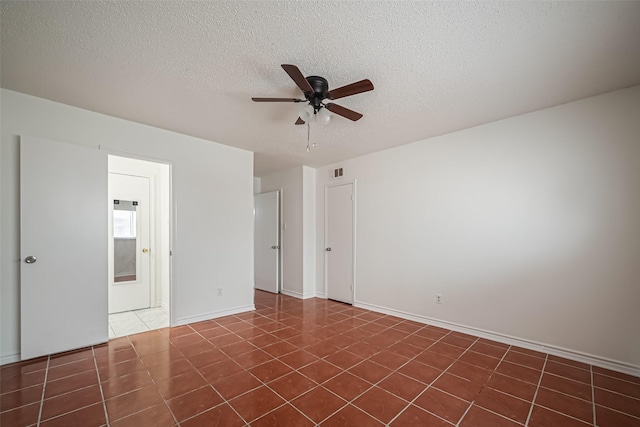 unfurnished room featuring a textured ceiling, dark tile patterned flooring, visible vents, a ceiling fan, and baseboards