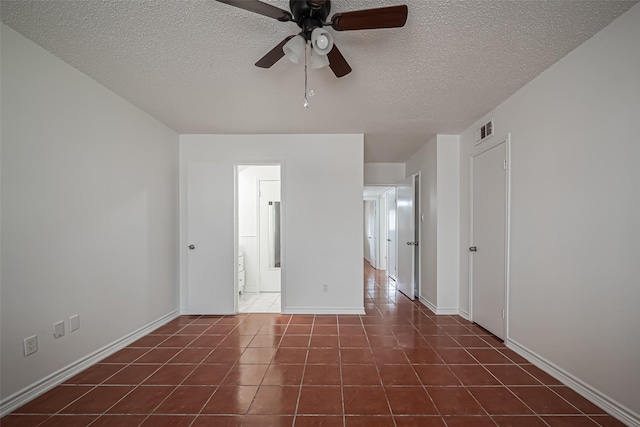 empty room with baseboards, visible vents, dark tile patterned flooring, ceiling fan, and a textured ceiling