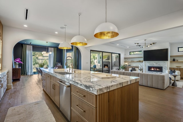 kitchen featuring stainless steel dishwasher, light brown cabinets, a sink, wood finished floors, and a lit fireplace