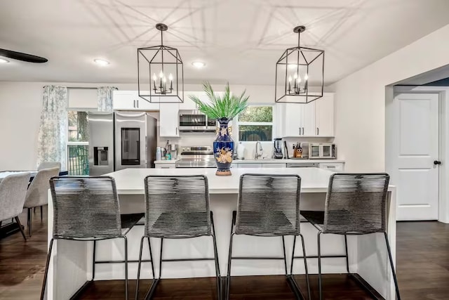 kitchen with appliances with stainless steel finishes, decorative light fixtures, light countertops, a kitchen bar, and white cabinetry