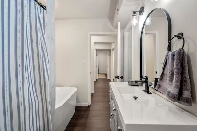 full bathroom featuring wood finished floors, a freestanding tub, vanity, and baseboards