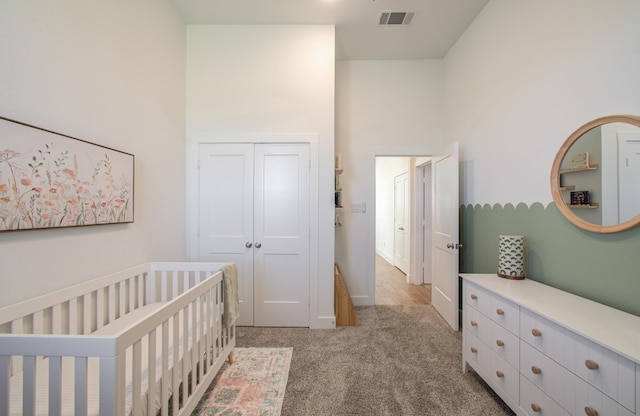 bedroom featuring a closet, visible vents, a towering ceiling, light carpet, and a crib