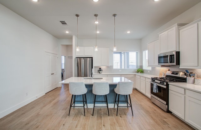 kitchen with a center island with sink, decorative light fixtures, stainless steel appliances, light countertops, and white cabinetry