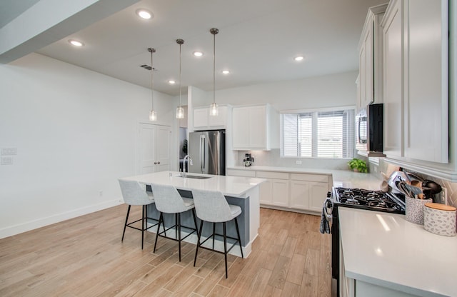 kitchen with a kitchen island with sink, white cabinets, light countertops, appliances with stainless steel finishes, and decorative light fixtures