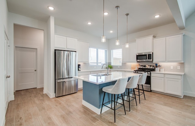 kitchen with a sink, white cabinetry, light countertops, appliances with stainless steel finishes, and a center island with sink