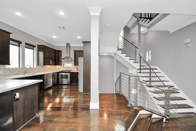 kitchen with stainless steel appliances, light countertops, dark brown cabinetry, and wall chimney exhaust hood