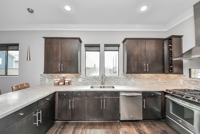 kitchen featuring stainless steel appliances, dark brown cabinets, wall chimney exhaust hood, and a sink