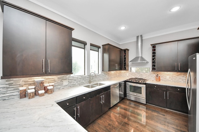 kitchen featuring dark brown cabinetry, stainless steel appliances, a sink, wall chimney exhaust hood, and tasteful backsplash