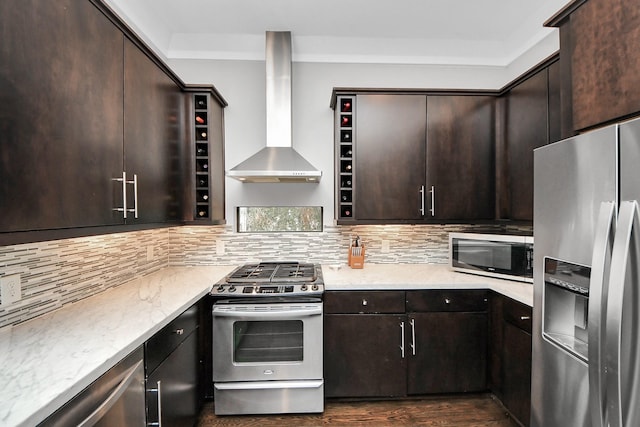 kitchen with dark brown cabinetry, wall chimney exhaust hood, stainless steel appliances, and decorative backsplash