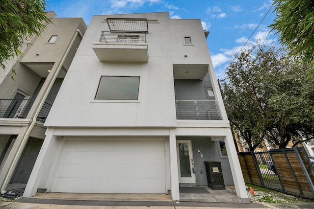 view of front facade featuring a garage, fence, a balcony, and stucco siding