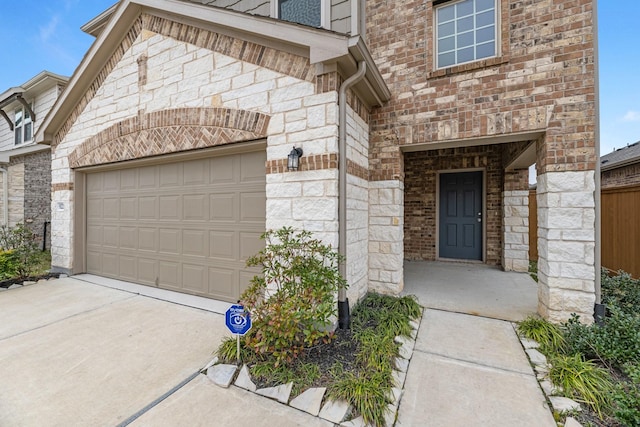 entrance to property featuring a garage, brick siding, and driveway