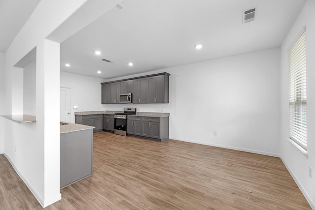 kitchen with visible vents, light stone counters, gray cabinets, stainless steel appliances, and light wood-type flooring