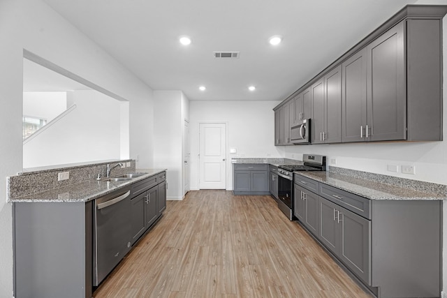 kitchen with light stone counters, a sink, appliances with stainless steel finishes, light wood-type flooring, and gray cabinets