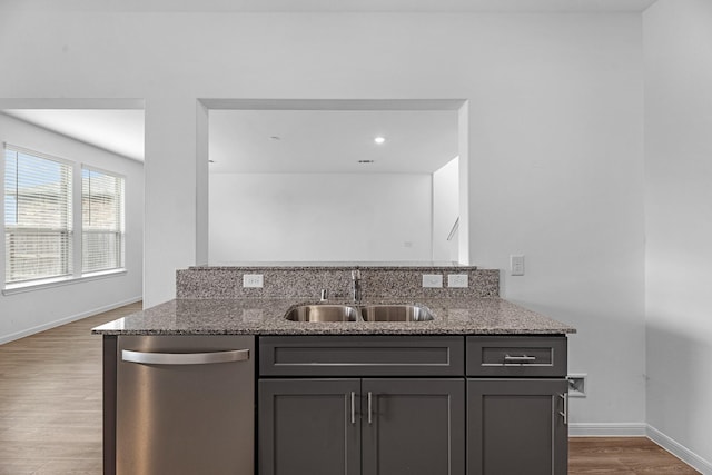 kitchen with baseboards, dishwasher, light stone counters, wood finished floors, and a sink