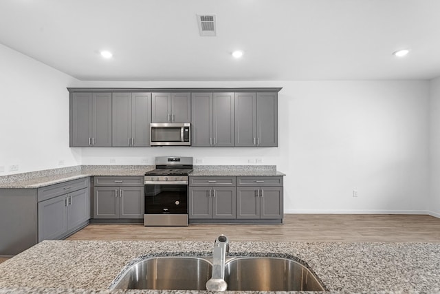 kitchen with stainless steel appliances, gray cabinets, a sink, and light stone counters