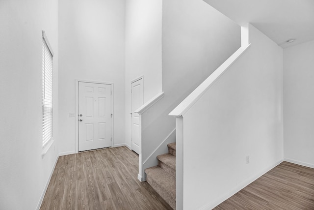 entryway featuring light wood-style floors, baseboards, stairway, and a high ceiling