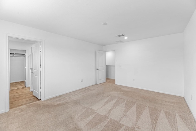 unfurnished bedroom with a closet, light colored carpet, visible vents, a spacious closet, and baseboards