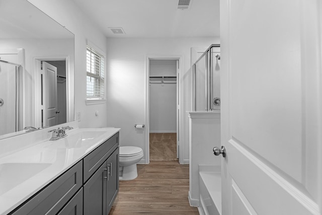 full bathroom with double vanity, visible vents, a shower stall, and wood finished floors