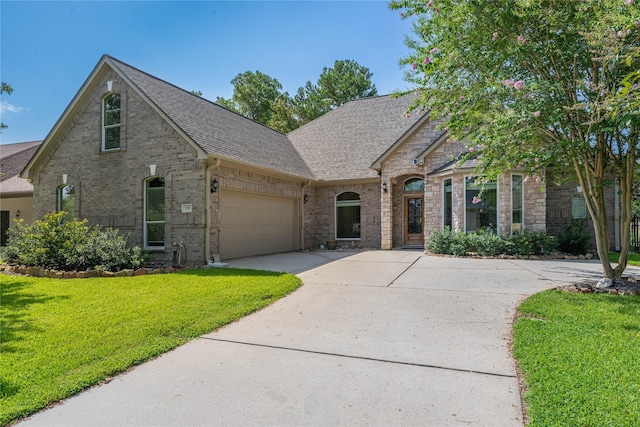 french country home with brick siding, roof with shingles, concrete driveway, a garage, and a front lawn