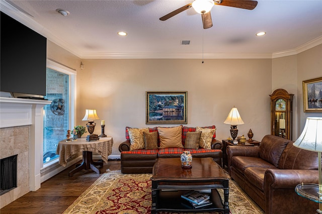 living area featuring dark wood-style floors, visible vents, ornamental molding, a ceiling fan, and a tile fireplace