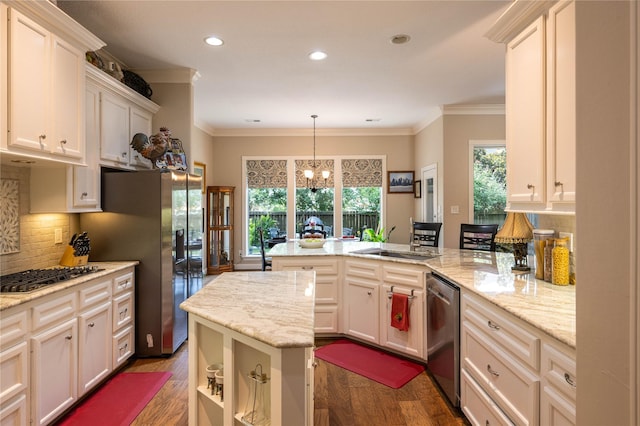 kitchen with a peninsula, stainless steel appliances, a sink, ornamental molding, and tasteful backsplash