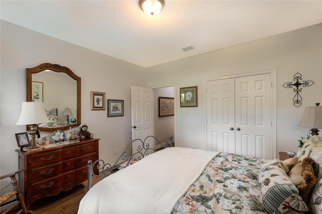 bedroom featuring dark wood-style floors, a closet, visible vents, and a textured ceiling