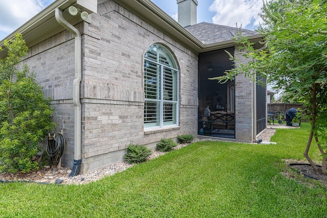 view of side of home featuring a yard, a chimney, fence, and brick siding