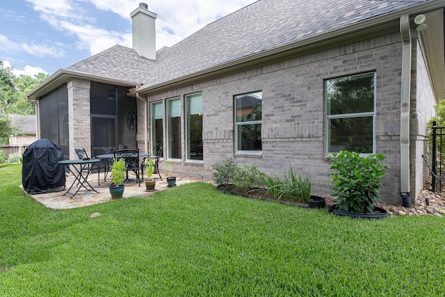 back of property with roof with shingles, brick siding, a chimney, and a lawn